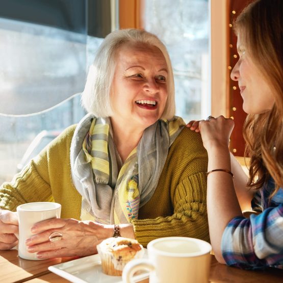 Photo of senior woman and daughter conversing in coffee shop.